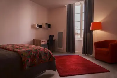a bedroom with a bed and a red chair and a window at La PARERIE 2 in Carcassonne