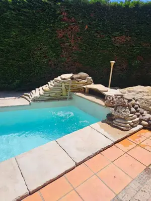 a swimming pool with a waterfall and a stone walkway at La Plénitude in Narbonne