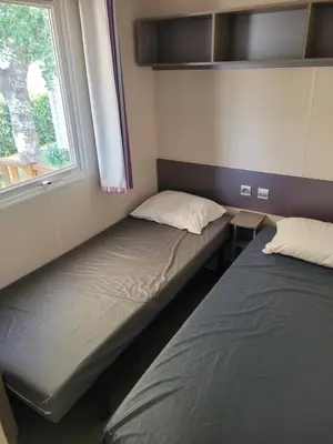 two beds sitting in a room with a window at mobile home climatisé, 3 chambres in Port-la-Nouvelle