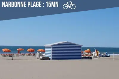 a blue building on a beach with chairs and umbrellas at Le Rivage du Nilautom in Gruissan