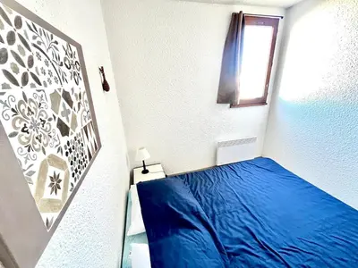 a small bedroom with a blue bed and a window at Lo Nidou Gruissan in Gruissan