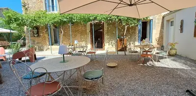 a patio with tables and chairs and an umbrella at Le MAS CLEMENTINE in Puisserguier