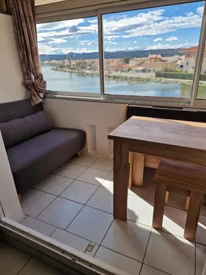 a table and bench in a room with a large window at Vue lac & mer à pied - Séjour détente in Port-la-Nouvelle