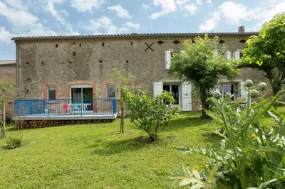 a large brick building with a blue balcony in a yard at Perets petit in Montégut-Lauragais