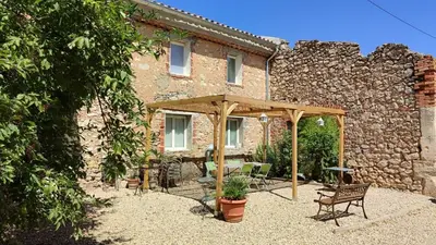 a patio in front of a brick building with a wooden canopy at Le gîte du moulin in Thézan-des-Corbières