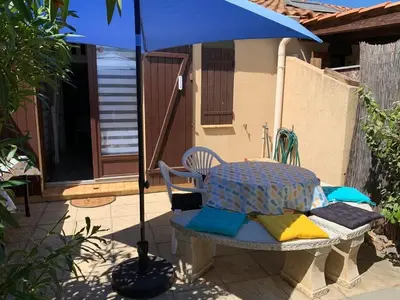 a table and chairs under an umbrella on a patio at Petite maisonnette de vacances in Gruissan