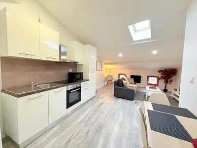 a kitchen with white cabinets and a living room at Le Refuge du Midi in Pamiers
