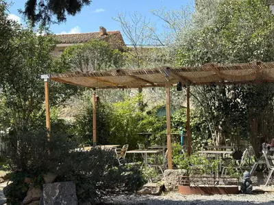 a wooden pergola with tables and chairs in a garden at O'MAZETTE CHAMBRE ROMANTIQUE VUE JARDIN AVEC PISCINE découverte de l'Aude in Fabrezan