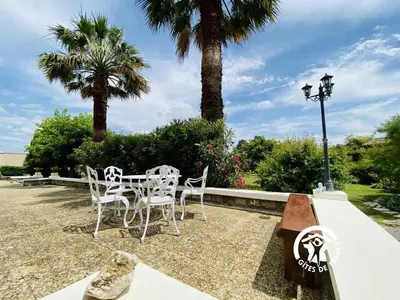 a patio with a table and chairs and palm trees at Au bien-etre in Villemoustaussou