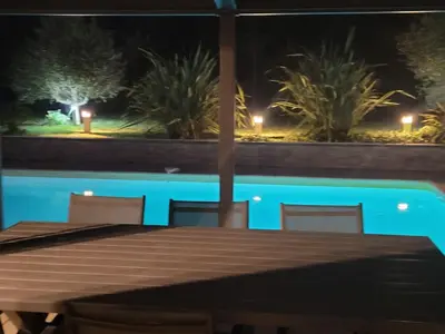 a wooden table with chairs and a pool at night at Villa Jade in Lasserre-de-Prouille