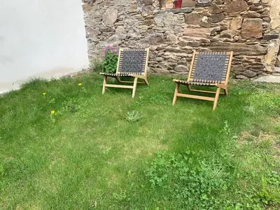 two chairs sitting in the grass next to a stone wall at La petite maison dans le Sidobre in Fontrieu