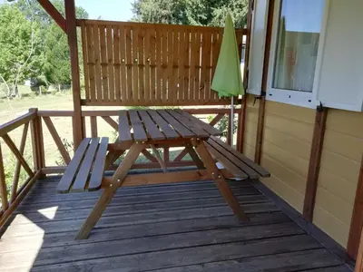 a wooden bench on a deck with an umbrella at Hébergement au Lac des Montagnès pour 5 personnes in Mazamet