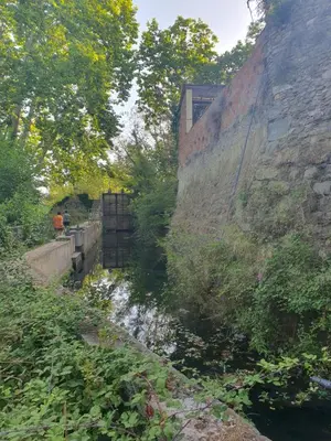 a river next to a stone wall with trees at Villa de l Ode in Mirepeisset