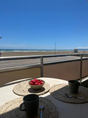 a table with two cups and a bowl of fruit on a balcony at APPARTEMENT Rénové de type 3 VUE MER in Port-la-Nouvelle