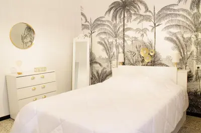 a bedroom with a white bed and palm trees wallpaper at Chez Céline, plein centre ville in Narbonne