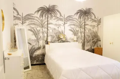 a bedroom with a white bed and palm trees mural at Chez Céline, plein centre ville in Narbonne