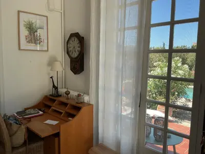 a room with a desk and a clock next to a window at Le Doul Jolie villa au calme climatisée grande piscine jardin in Peyriac-de-Mer