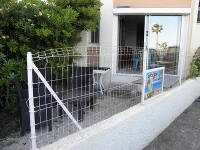 a fence in front of a house with a dog at Appart RDC avec cour à 60 m plage du Grazel Gruissan in Gruissan