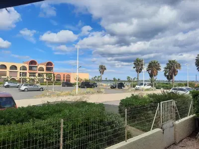 a parking lot with palm trees and a building at Appart RDC avec cour à 60 m plage du Grazel Gruissan in Gruissan