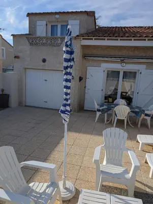 a patio with white chairs and a blue and white umbrella at Maison de vacances climatisée 600m de la mer Cour privative et parking in Port-la-Nouvelle