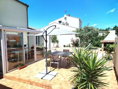 a patio with a table and an umbrella at Lumineuse villa au pied de la pinède in Lézignan-Corbières