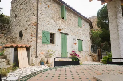 a stone building with green shuttered windows and a patio at Volet verts 8 personnes in Fitou
