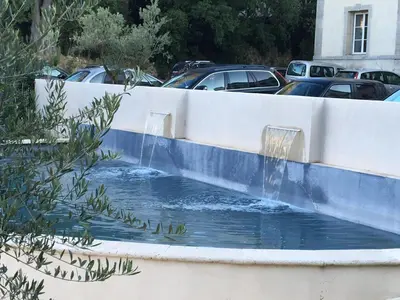 a water fountain in a retaining wall with cars parked at La Redorte 23 in La Redorte