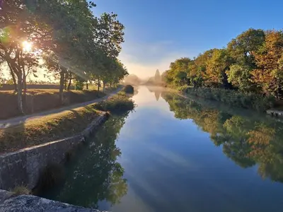 a view of a river with the sun shining on it at Le nid du canal in Pezens