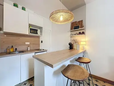 a kitchen with white cabinets and a counter with stools at Le BEHNA - Wi-Fi Apartment - Air Conditioning in Narbonne
