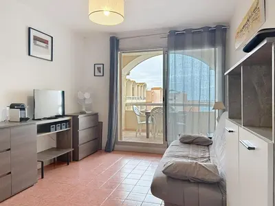 a kitchen with a couch in a room with a balcony at Le Thalio - Swimming pool - Air conditioning in Gruissan