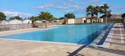 a large blue swimming pool with a fence and palm trees at El sol in Port-la-Nouvelle