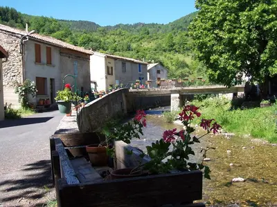 a village with a river with flowers and a bridge at Vacances en pays cathare réservable du samedi au samedi les mois de Juillet et Aout in Joucou