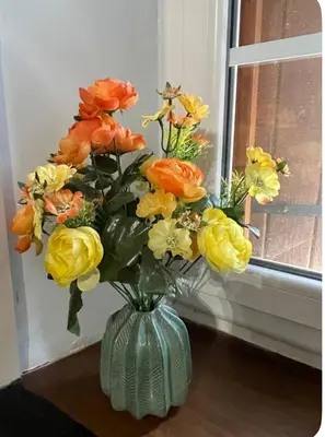 a green vase filled with yellow and orange flowers at Bienvenue chez Sandrine in La Redorte