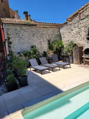 a patio with lounge chairs next to a brick wall at Gîte de la tour avec piscine entre Carcassonne et narbonne in Capendu