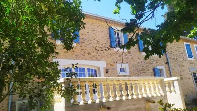 a stone house with a white balcony and trees at Château de Prax Viel - piscine et mini ferme, climatisé in Lagrasse