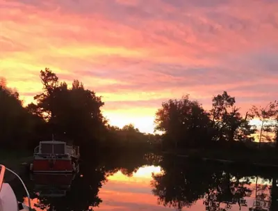 a sunset over a river with a boat in the water at bateau tinkerbell in Labastide-dʼAnjou