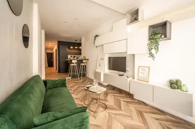 a living room with a green couch and a kitchen at L'Appart Central - Chic et Confort in Narbonne