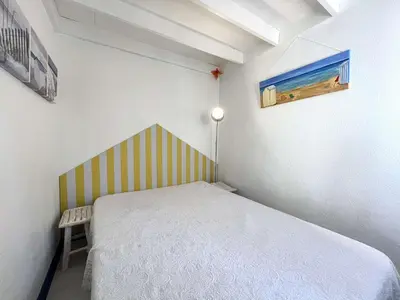 a small bedroom with a bed with a striped headboard at Appartement La Pinède avec Terrasse, clim et parking - GN320-124 in Gruissan