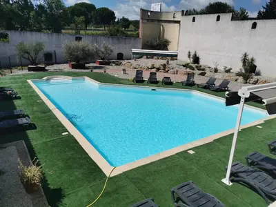 a large swimming pool in a yard with chairs at Hôtel Le Floreal in Trèbes