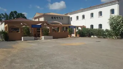 a building with a parking lot in front of it at Hôtel Le Floreal in Trèbes