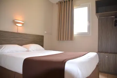 a bedroom with a large bed with a window at Hôtel Le Floreal in Trèbes