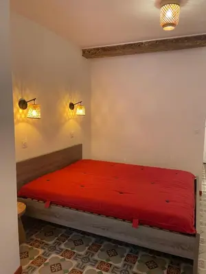 a bedroom with a red bed with two lights on the wall at Appartement avec jardin sous les couverts in Mirepoix