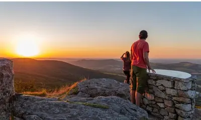 a man and woman standing on top of a rock wall watching the sunset at Magnifique Gîte 4 à 10 personnes in Nages