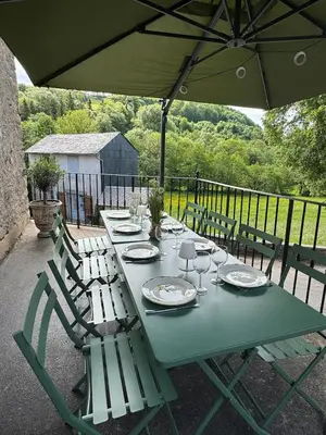 a green table with chairs and an umbrella at Magnifique Gîte 4 à 10 personnes in Nages