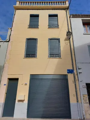 a yellow building with a garage door and four windows at Jolie maison de village avec vue in Maury