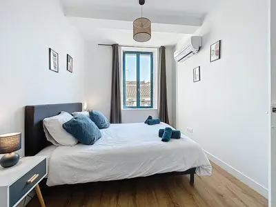 a bedroom with a bed with blue pillows and a window at L'Alcazar - Appartement à deux pas des halles - Climatisation in Narbonne