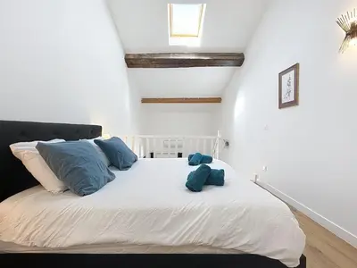 a bedroom with a white bed with blue pillows at Le Datrio - Appartement proche des halles - Wifi et climatisation in Narbonne