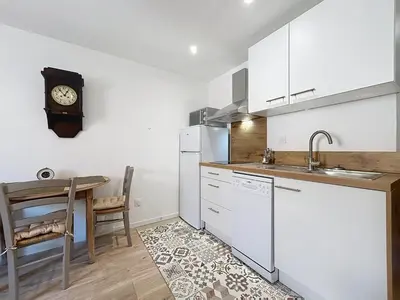 a kitchen with a table and a clock on the wall at Le Lies - Appartement proche de la mer in Salles-d'Aude