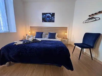 a bedroom with a large bed and a blue chair at La Saphir in Narbonne