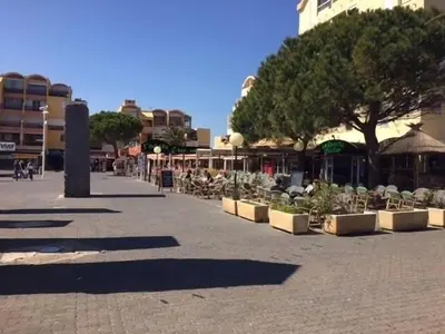 a street with chairs and trees on a sidewalk at Au cœur du village de Gruissan in Gruissan